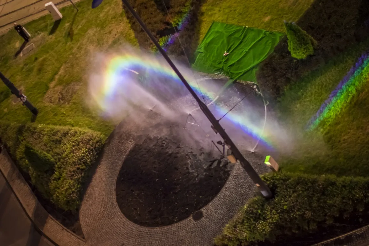 Rainbow prism cast across a wet circular roadway and grass